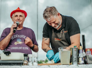 A chef cutting onions on a cutting board with a commentator behind his back