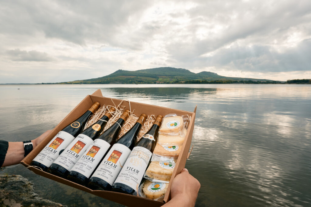 Tasting box with five bottles of wine and cheese photographed above the surface, Palava can be seen in the background