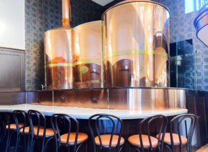 Three copper beer stills in the Efi brewery with standing chairs around