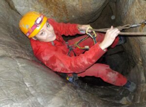 A lady in overalls abseiling down into the bowels of a cave on a speleofera