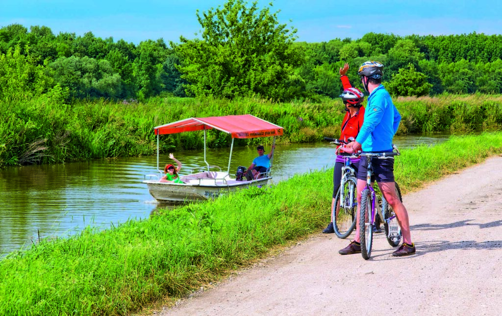Cyclists salute a boat on the Bata Canal with a red streak
